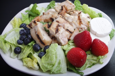 chicken salad on lettuce with blueberries and strawberries, served on a white plate