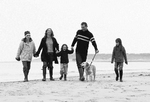 family with 3 children (girls) walking dog along shore
