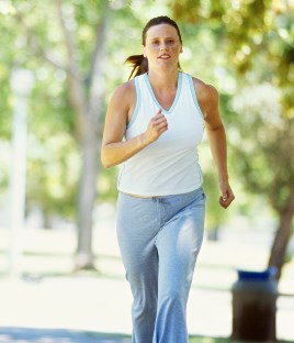 woman wearing light blue tank top jogging in wooded area