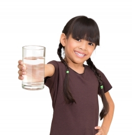 10 year old girl with pigtails, holding a clear glass of water toward viewer