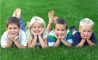 4 children about 9 years old lying on tummies on grass, chins cupped in their hands